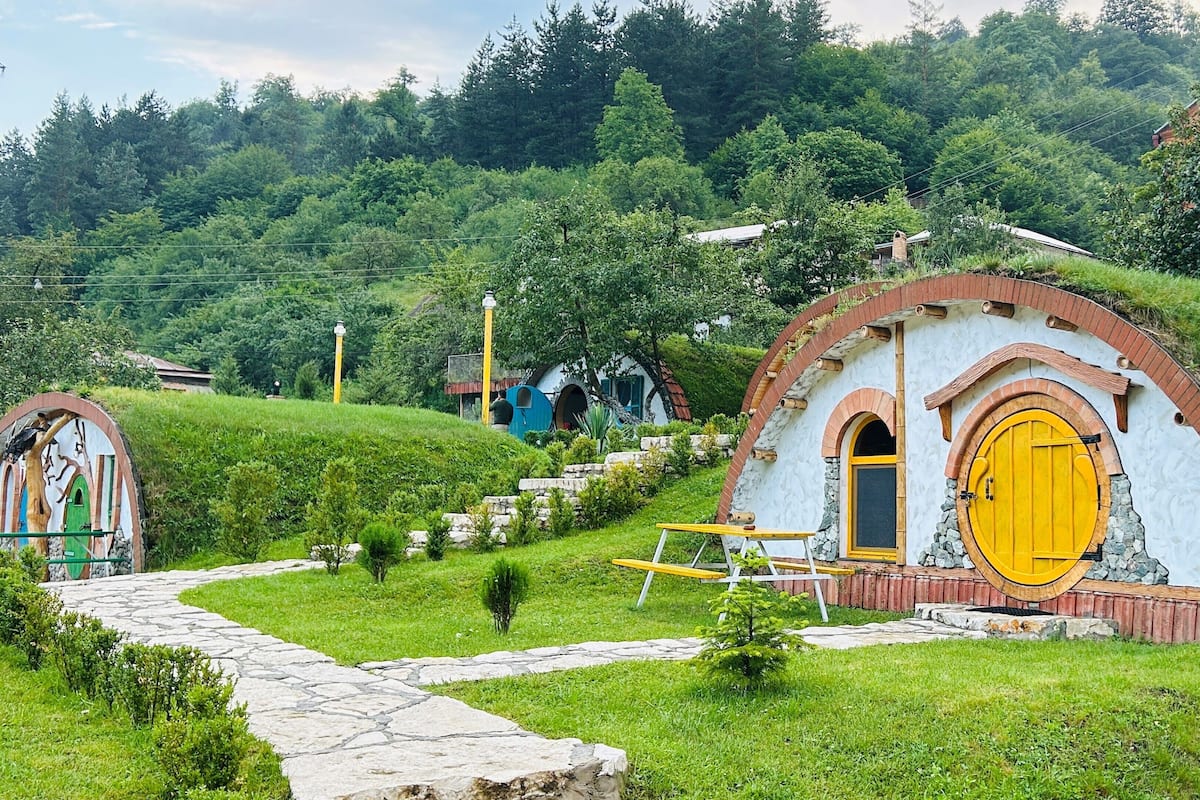 A rural setting with a stone pathway leading to a house with a yellow door and a stone wall.