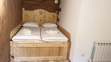 En træseng med to puder og sammenfoldede håndklæder, en radiator og et flisegulv.
