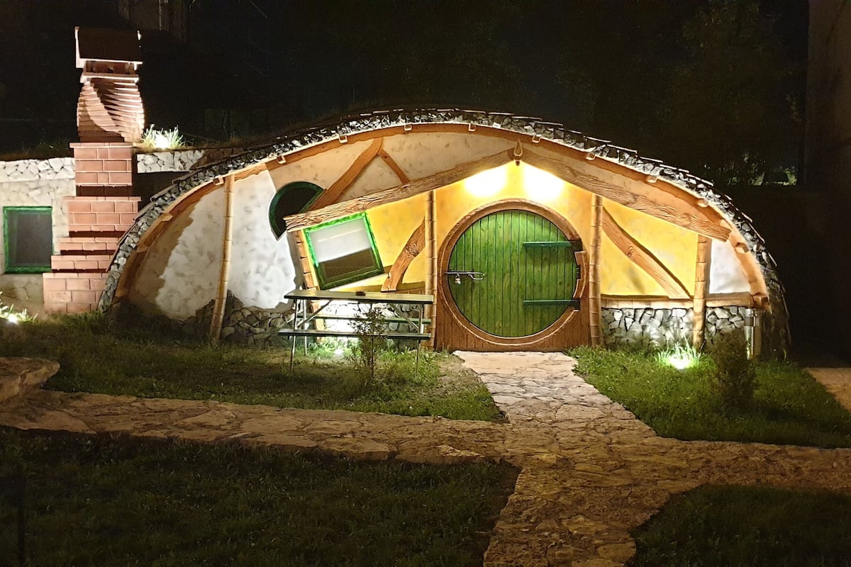 A Hobbit-style tent with a green door and a small table in front, surrounded by stone steps and grass.