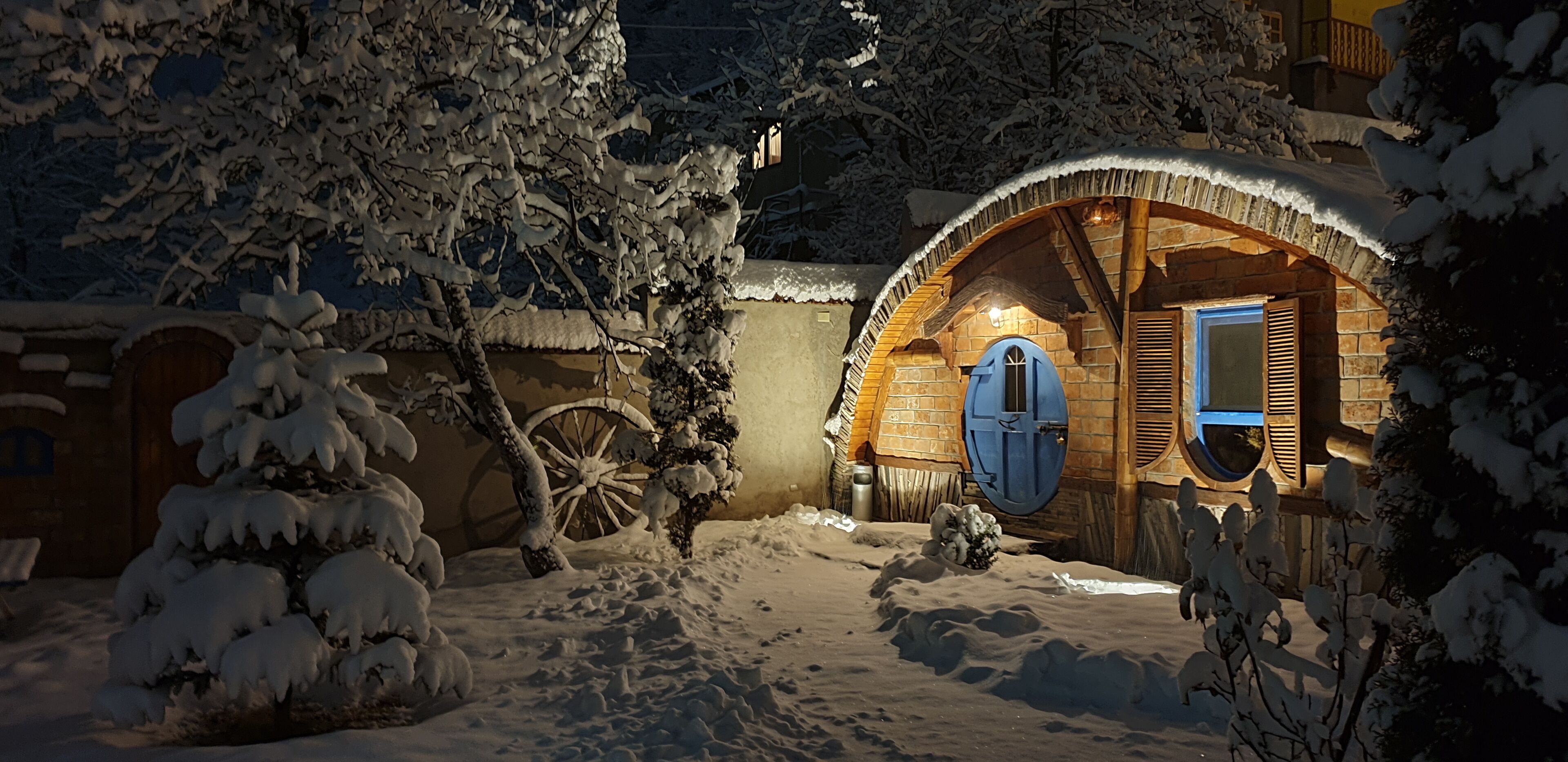 Una cabaña cubierta de nieve con fachada de madera, una puerta azul y un carretón en primer plano.