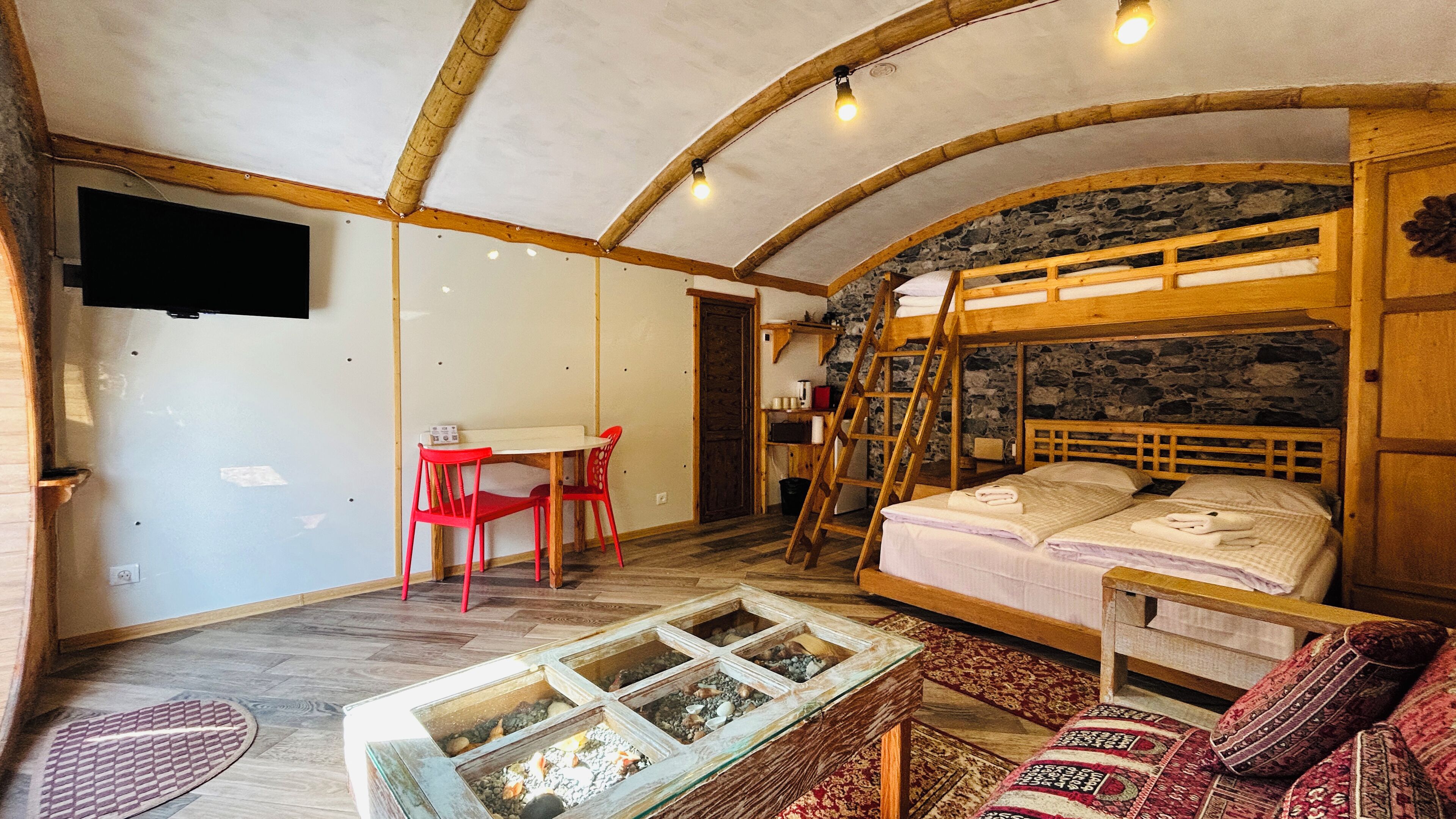 Una habitación rústica con literas, un escritorio con silla, una mesita con un adorno y una alfombra estampada.