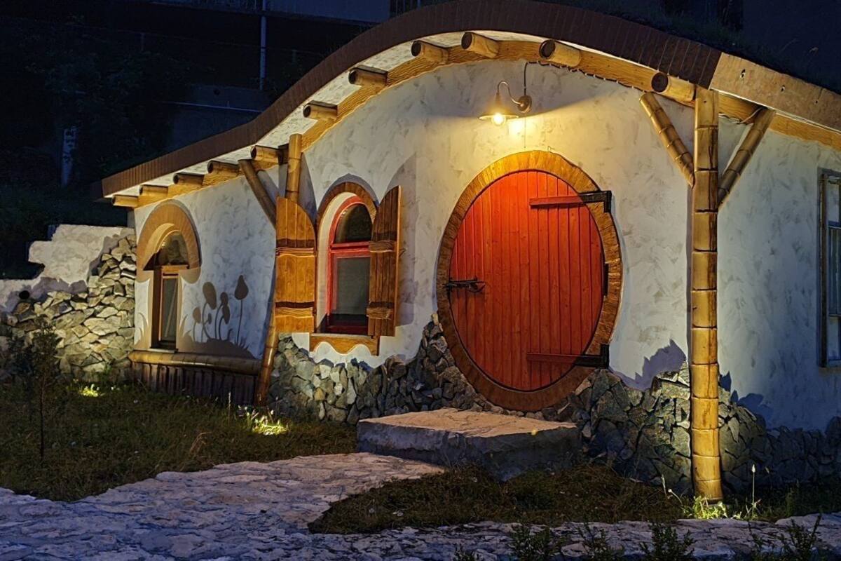A rustic house with a stone foundation, wooden arches, and a red door.