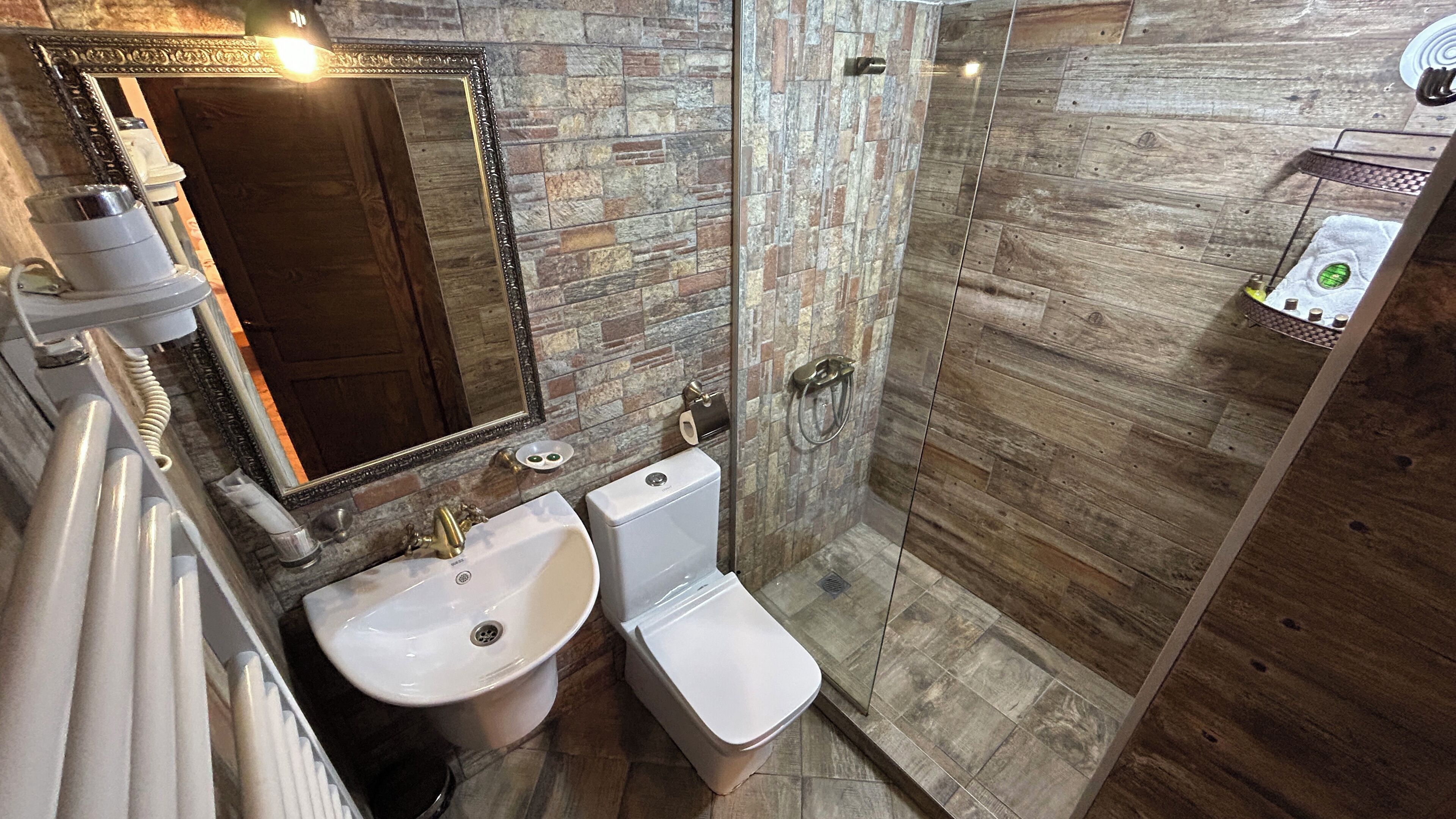 Een badkamer met een stenen muur, een spiegel, een wastafel, toilet en douche.