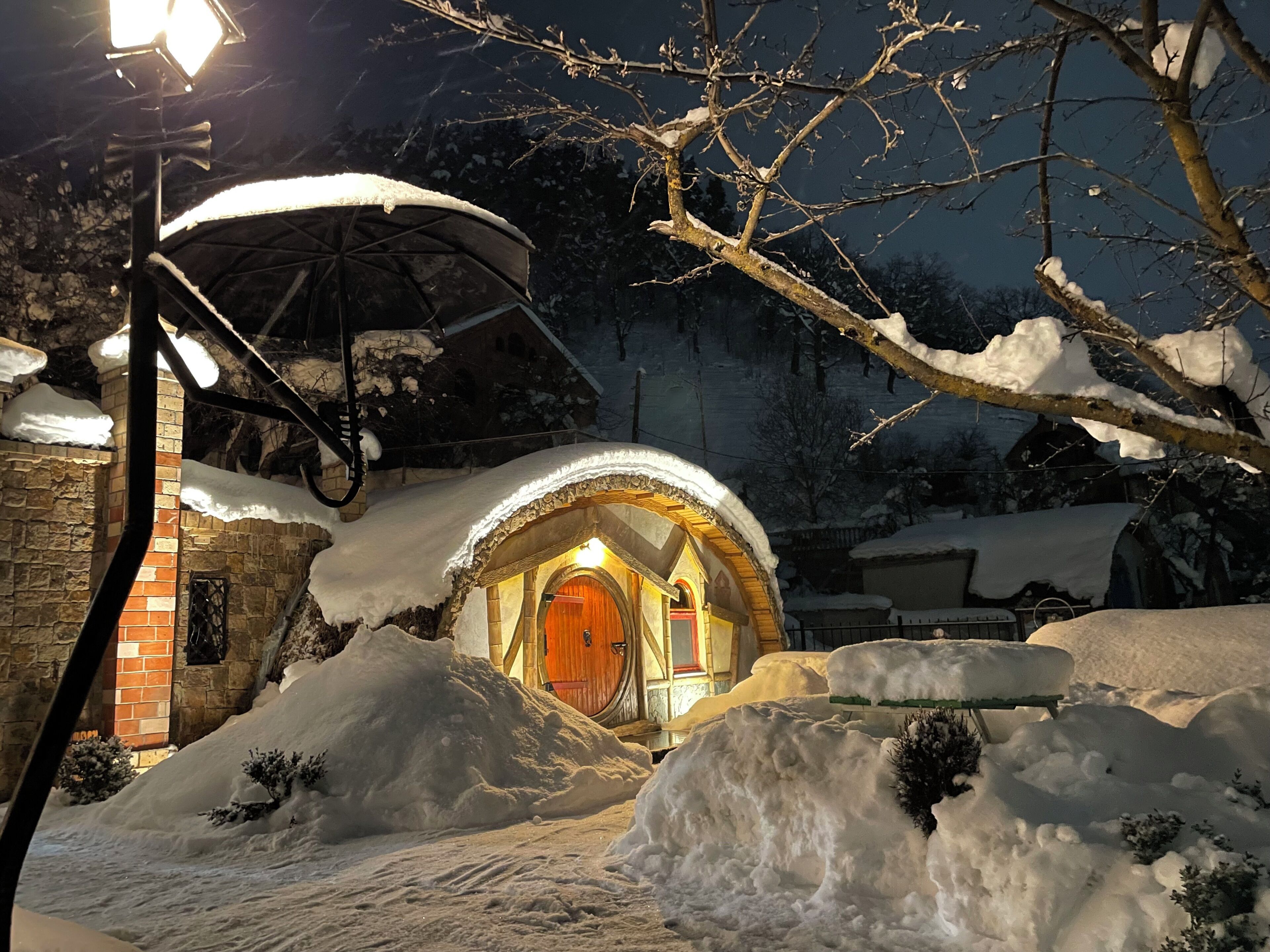 A snow-covered courtyard with a wooden structure featuring an arched entrance and a lit interior.
