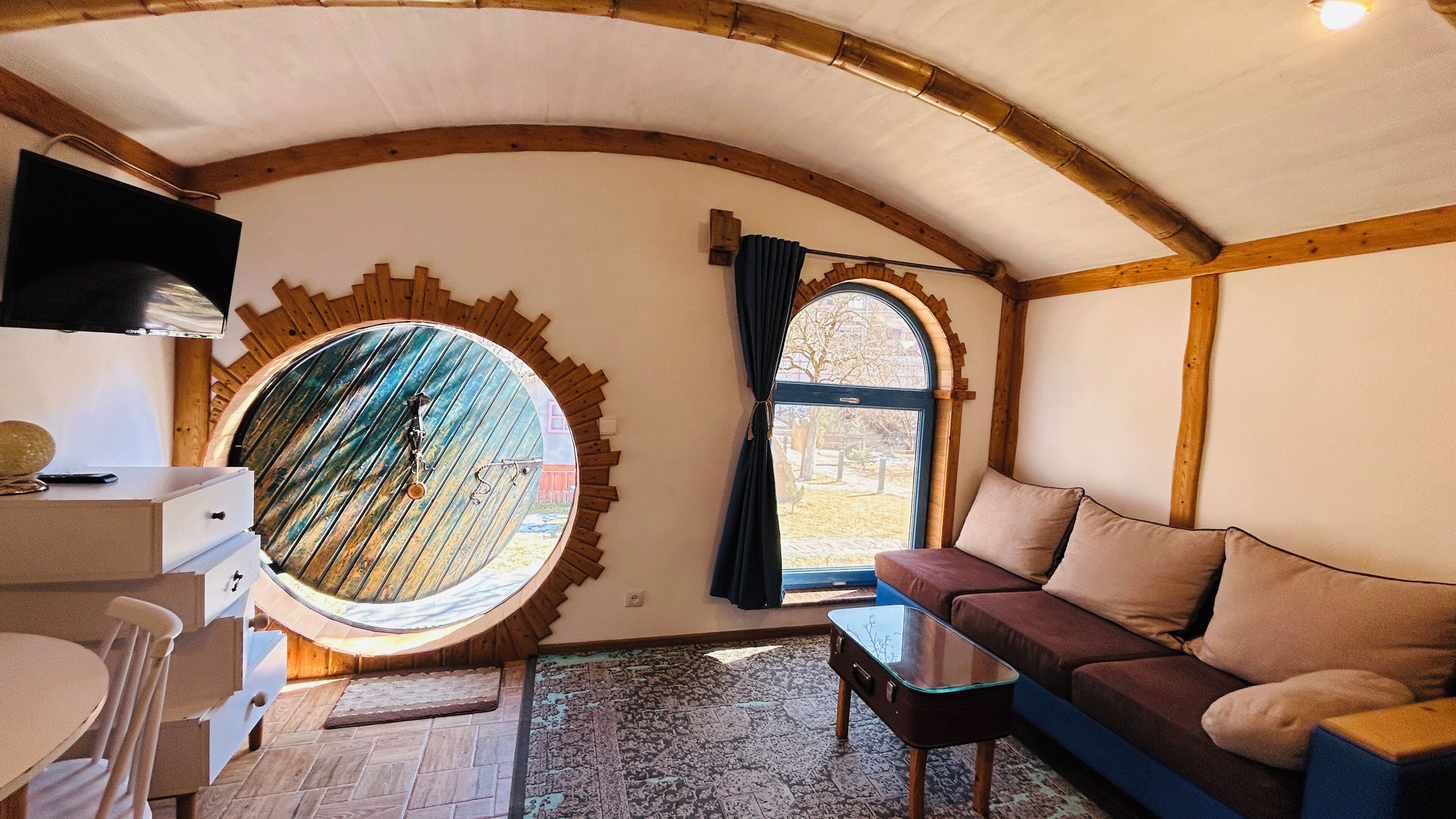 A cozy room with a round window, a sofa, a small table, and a TV on a stand.