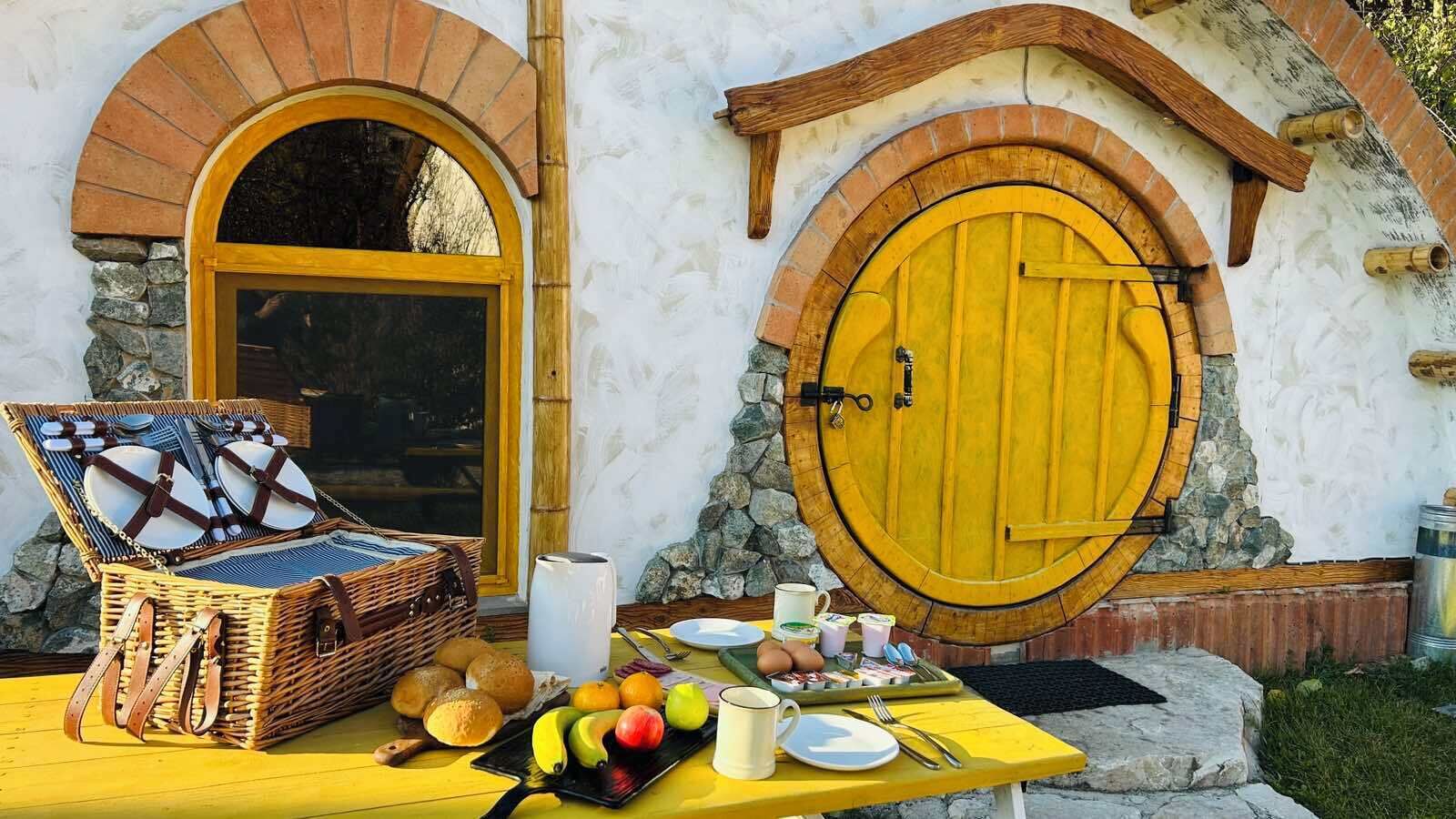 Una mesa dispuesta con comida y una cesta, una puerta amarilla y un muro de piedra.
