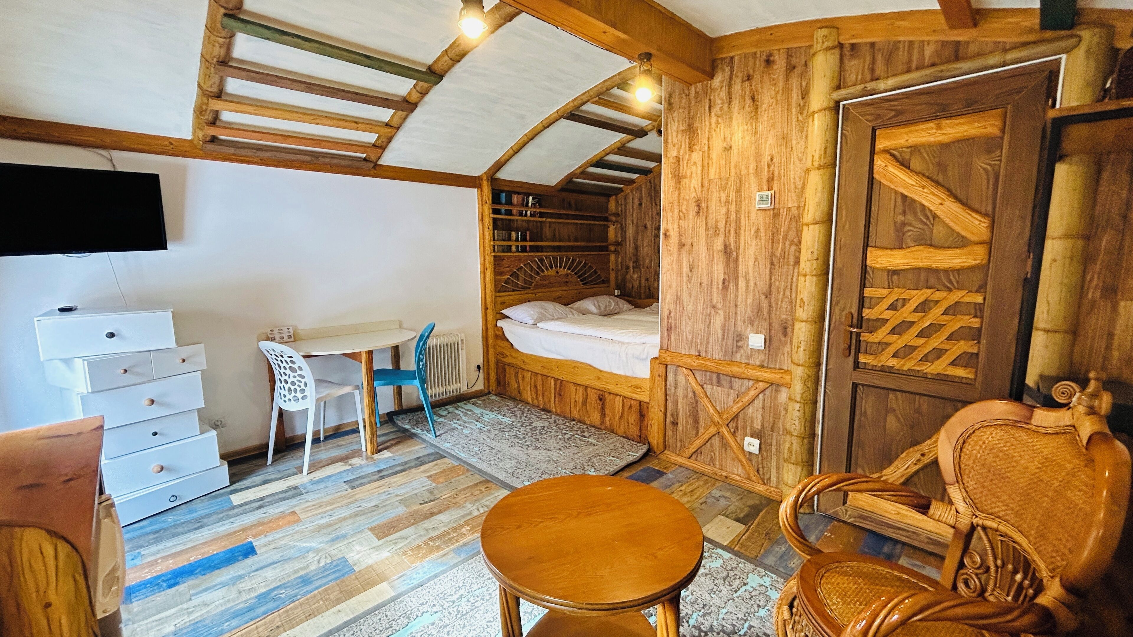 A room with a bed, a table, chairs, a dresser, and a television.
