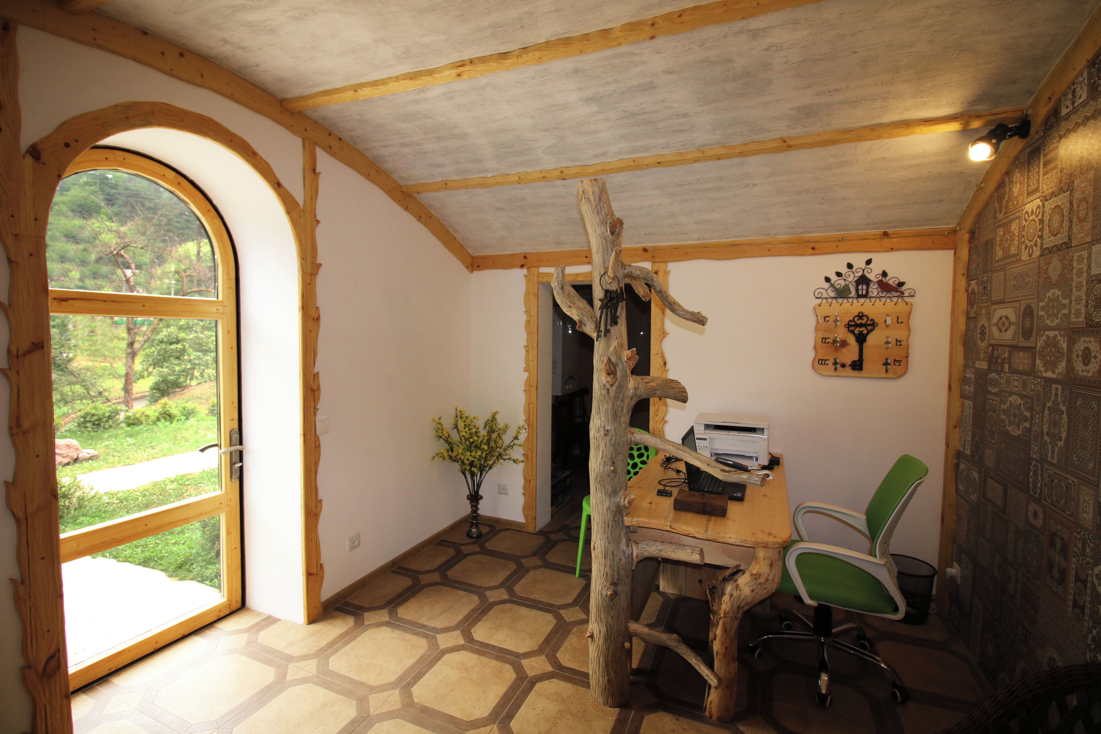 Una habitación rústica con un escritorio de madera, una silla verde, un ventanal grande y una decoración de pared original.