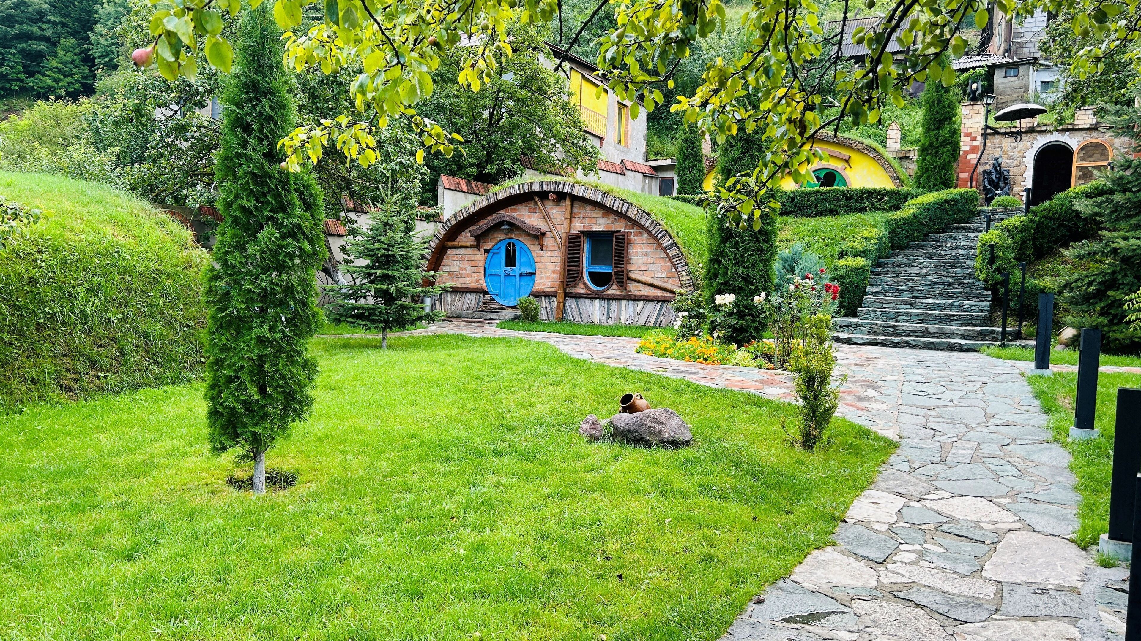 Una cabaña encantadora con puerta azul, rodeada de abundante vegetación y un sendero de piedra.