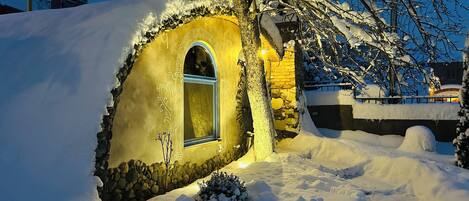 A snow-covered house with a circular window and a stone wall.