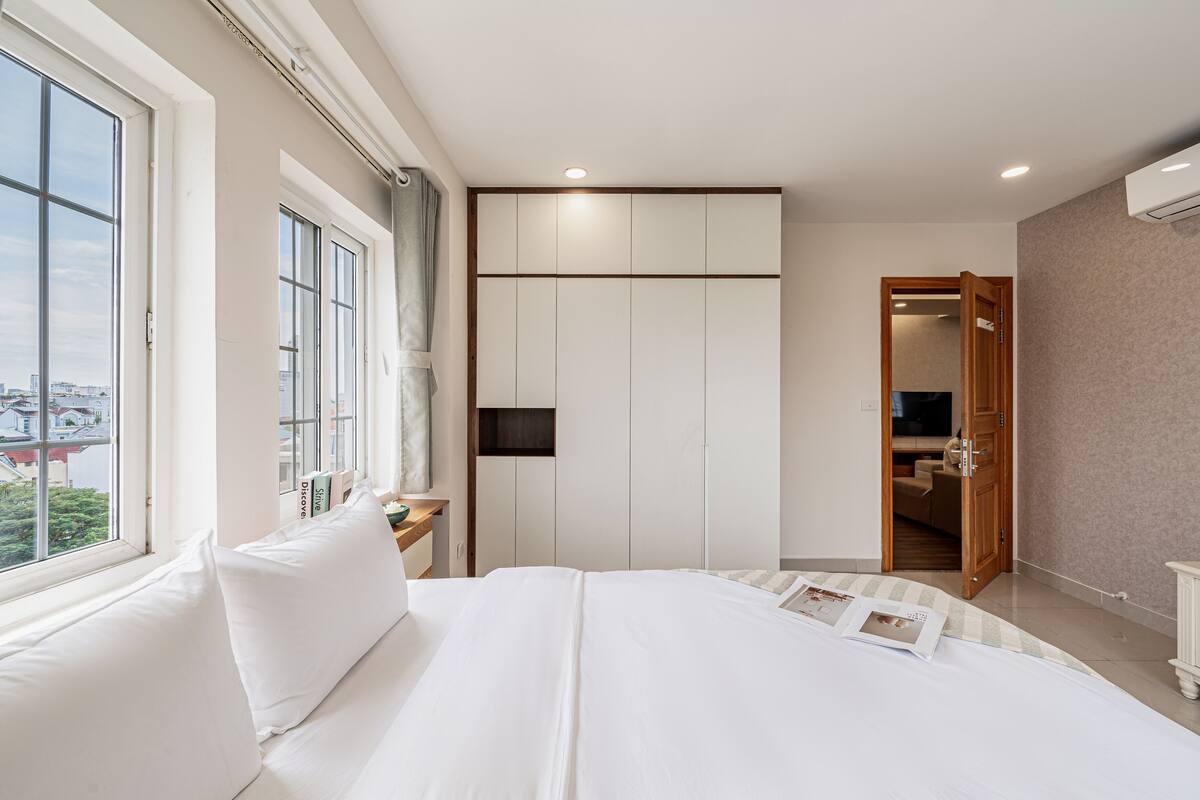 Un dormitorio moderno con una cama grande, un armario, un televisor y vistas a la ciudad desde la ventana.