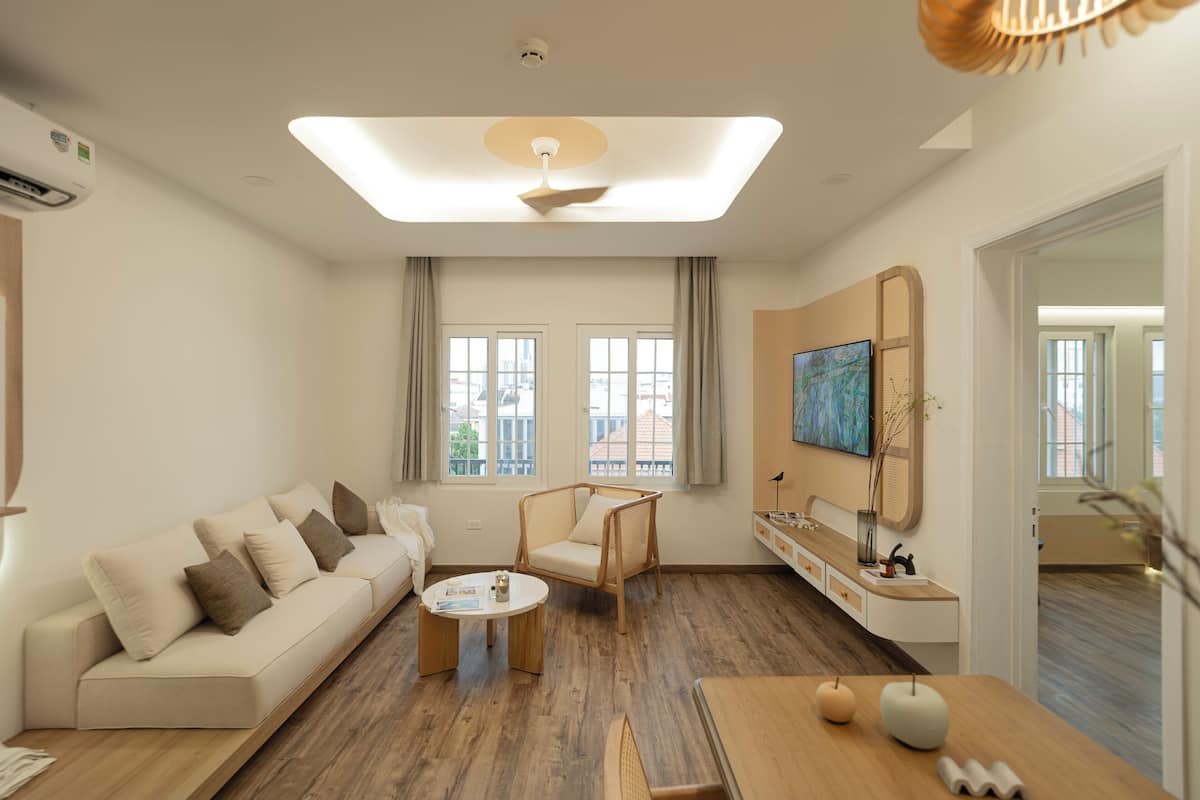 Una sala de estar moderna con un sofá, una mesa de centro, una silla, un televisor montado en la pared y un ventanal con cortinas.