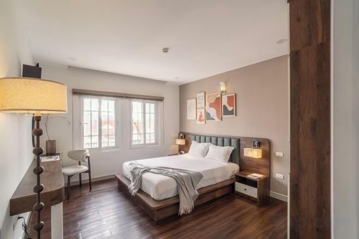 A bedroom with a bed, bedside tables, a chair, a lamp, and artwork on the wall.