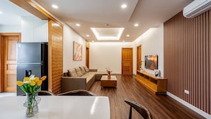 Un salon moderne comprenant un coin repas, un plancher en bois, un luminaire au plafond et un téléviseur fixé au mur.
