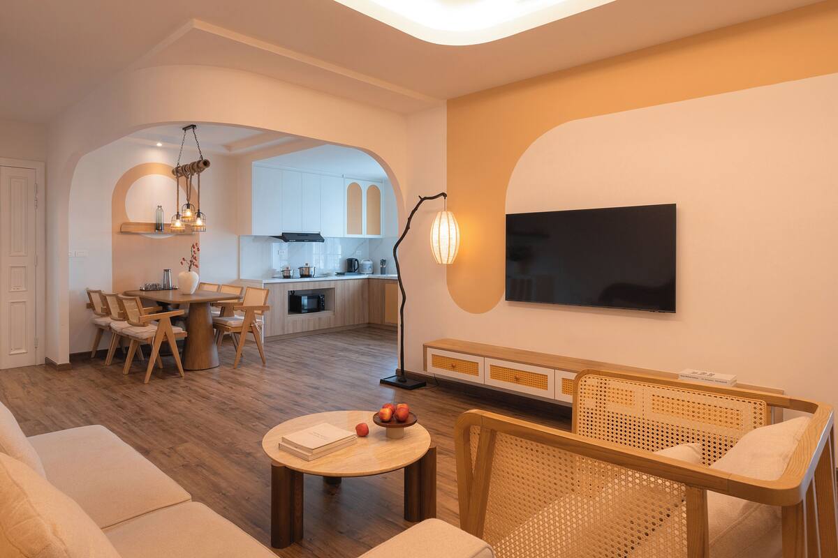 Una sala de estar moderna con un sofá, una mesa de comedor con sillas, una zona de cocina con televisor y un diseño de techo único.