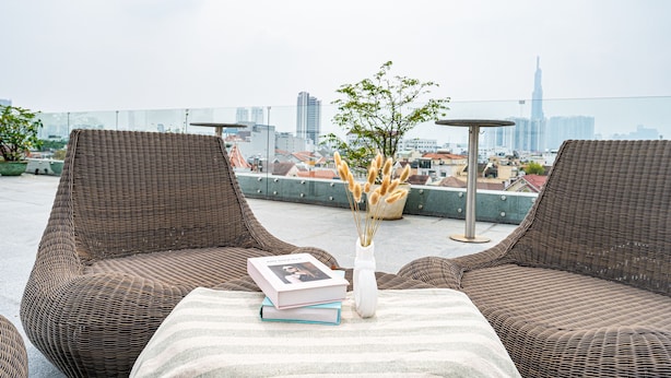 Une terrasse sur le toit, avec des fauteuils en osier, une table avec des livres et un vase, et une vue sur la ville.