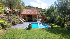 A backyard with a swimming pool, a covered patio area with chairs, and a stone wall.