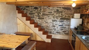 A kitchen with a stone wall, wooden staircase, and a dining area with benches.