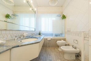 Features a double sink and pedestal sink, with a sleek countertop and natural light from large windows.