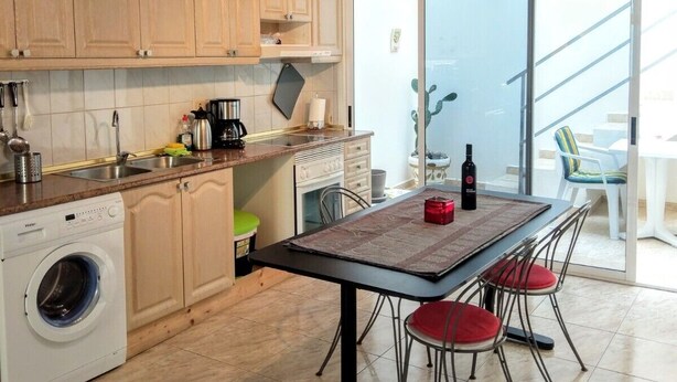 A kitchen with wooden cabinets, a washing machine, a dining table with chairs, and a view of the outside through a glass door. - Arguineguin, vacation home directly by the sea, Casa Perchel (Arguineguin)