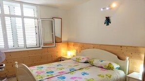 A bedroom with a wooden headboard, a bed with floral bedding, a bedside table, and a window with blinds. - Arguineguin, vacation home directly by the sea, Casa Perchel (Arguineguin)