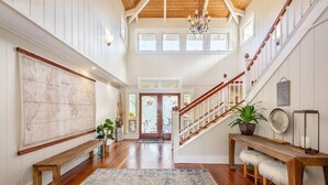 A spacious foyer with a wooden staircase, a large map on the wall, and a bench. - Napali Sunset Views+Pool/Spa + Bali Hai (Princeville)