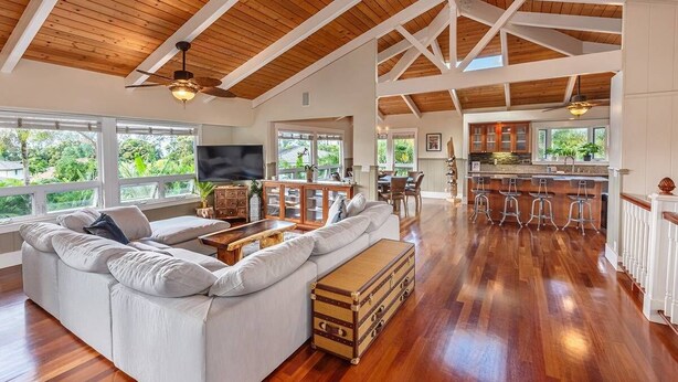 A spacious living area with a large sofa, wooden flooring, and a kitchen in the background. - Napali Sunset Views+Pool/Spa + Bali Hai (Princeville)