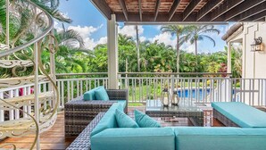 A covered outdoor seating area with wicker furniture and cushions, overlooking a pool and lush greenery. - Napali Sunset Views+Pool/Spa + Bali Hai (Princeville)