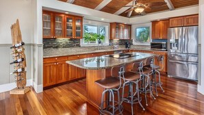 A spacious kitchen with wooden cabinets, a large island with bar stools, and a stainless steel refrigerator. - Napali Sunset Views+Pool/Spa + Bali Hai (Princeville)