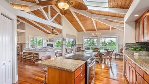 A spacious kitchen with wooden beams, a central island, and a view of the outdoors. - Napali Sunset Views+Pool/Spa + Bali Hai (Princeville)