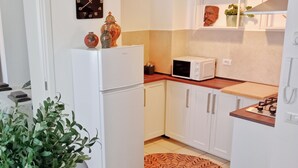 A compact kitchen with white cabinets, a white refrigerator, a microwave, and a gas stove. There is a patterned rug on the floor and a potted plant in the corner. - Cozy apartment in historic country residence, between Perugia and Assisi (Perugia)