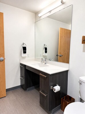 Ein modernes Badezimmer mit Waschbecken in Weiß, dunklem Holzschrank, großem Spiegel und Toilette.