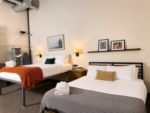 Ein Hotelzimmer mit zwei Betten, einem Schreibtisch, einem Stuhl, einer Lampe und einem Regal mit Bildern.