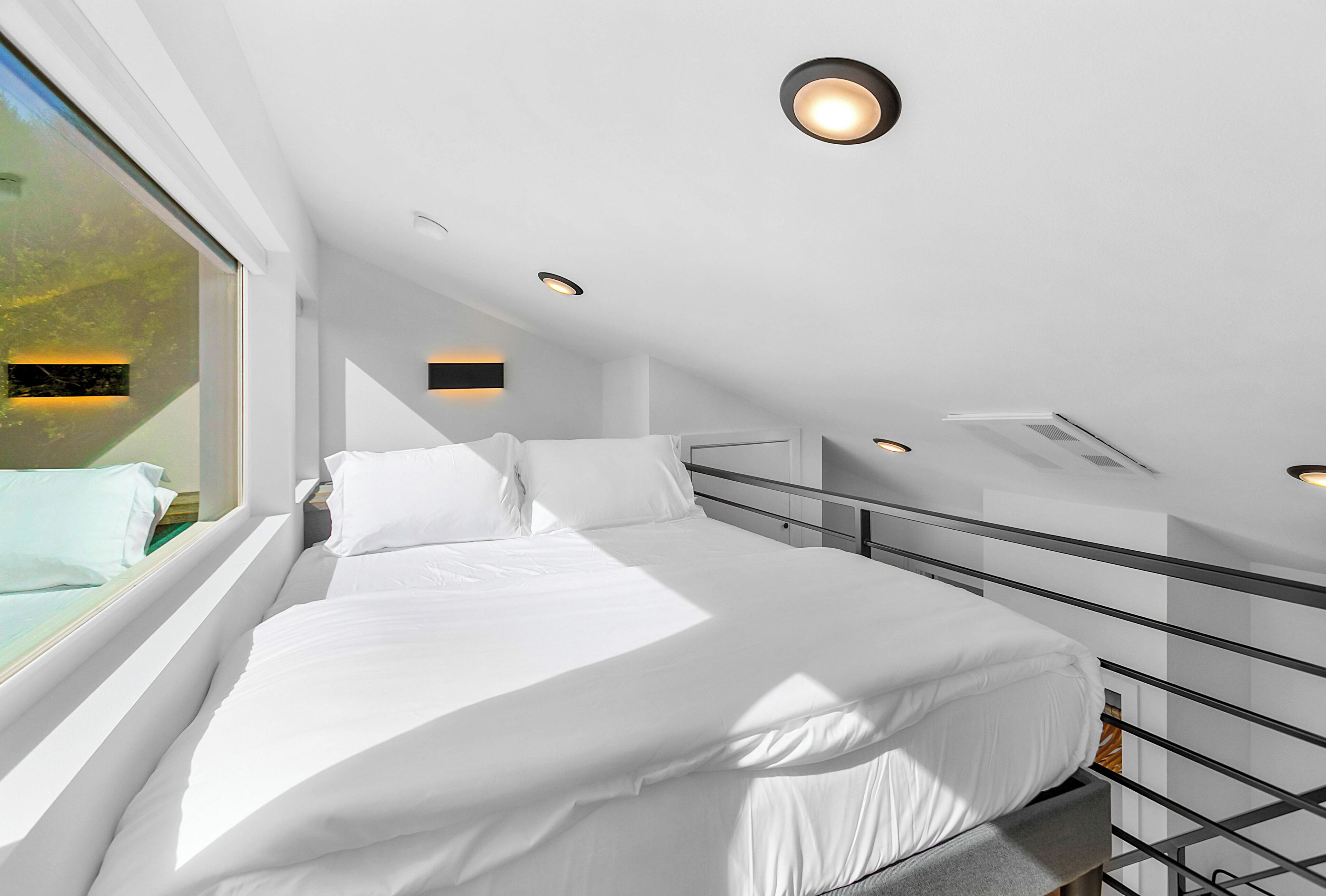 A modern, well-lit bedroom with a large bed, a window with a view of greenery, and a skylight.