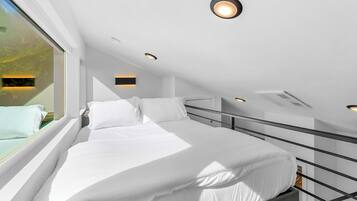 A modern, well-lit bedroom with a large bed, a window with a view of greenery, and a skylight.