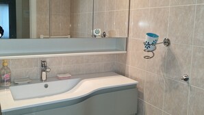 A bathroom with a white sink, a mirror with lights, and beige tiles.