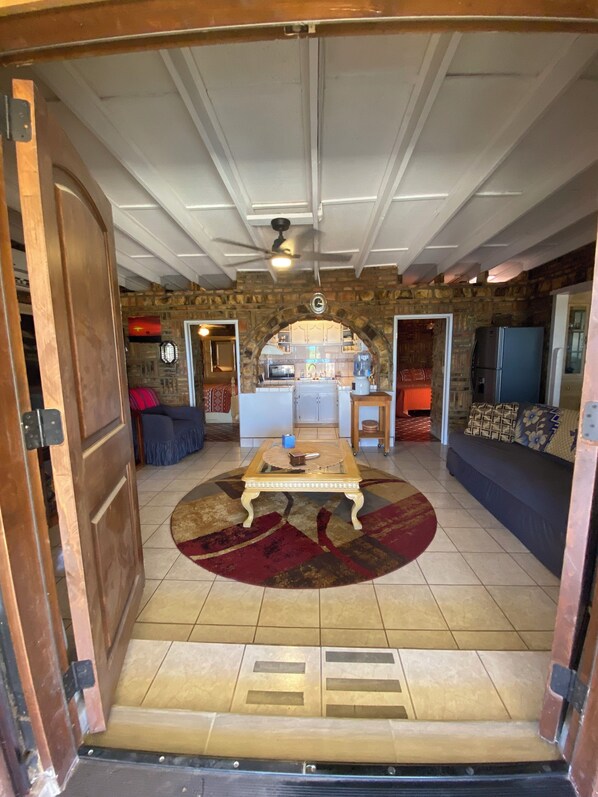An open doorway to a living room with a stone wall, a ceiling fan, a coffee table, and a sofa. - Charming 2-bedroom house one block to beach 5 minutes to town (San Felipe)