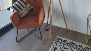 A modern living room with a large window, an orange armchair, a floor lamp, and a patterned rug. - Balcony View Apartment- Sleeps 5 & Private Parking (Solihull)