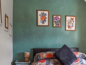 Une chambre à coucher comprenant un lit, une table de chevet, une lampe et trois œuvres d’art florales encadrées accrochées au mur.