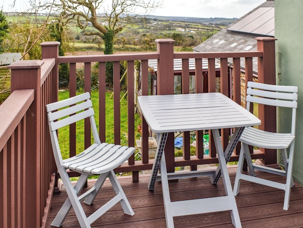 A balcony with a table and two chairs, overlooking a green landscape.