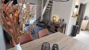 A modern dining area with a wooden table, two black candle holders, and a vase with dried plants.
