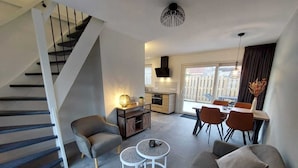 A modern living room with a staircase, a dining area, and a kitchen.