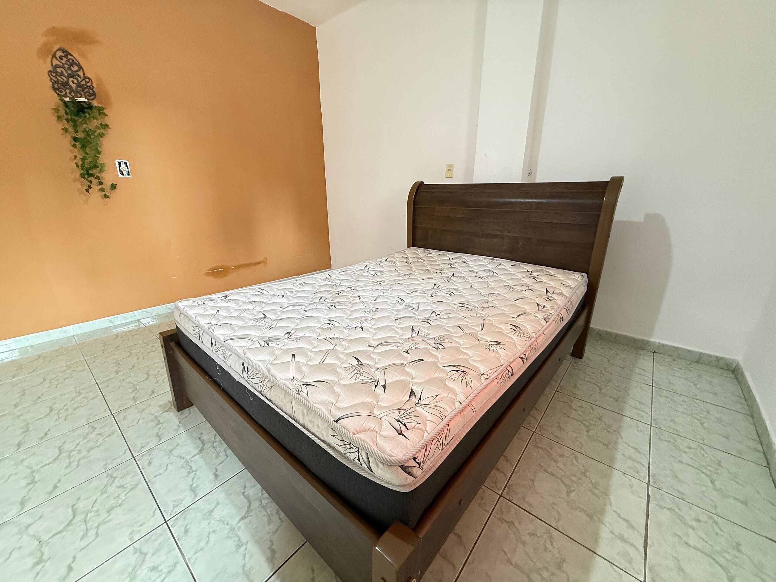 Un lit simple avec un matelas à motifs floraux, dans une pièce aux murs orange et au sol carrelé.
