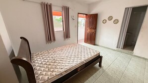 Een slaapkamer met een bed, gordijnen, een deur en een betegelde vloer.