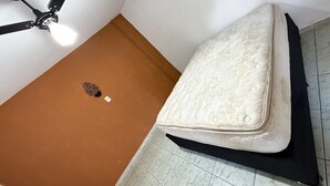 Een kamer met een plafondventilator, een matras op de vloer en een bruine muur.