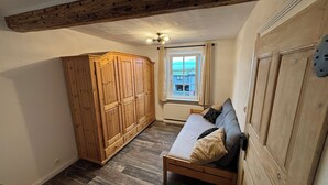 Un dormitorio con un armario de madera, una cama con almohadas, una ventana con cortinas y una viga de madera en el techo.