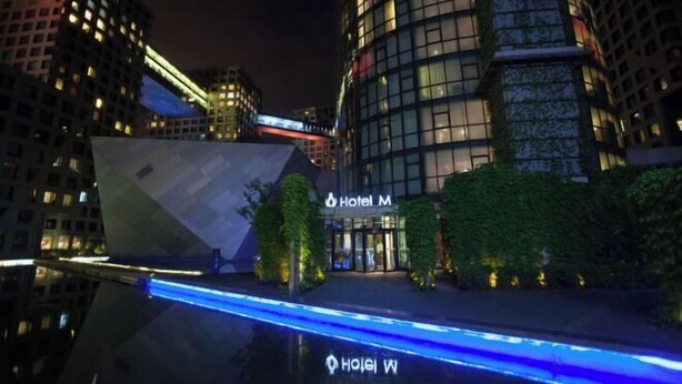 A modern hotel with a prominent glass facade, a well-lit entrance, and a pool area with blue lighting. - Hotel MoMc (Beijing)
