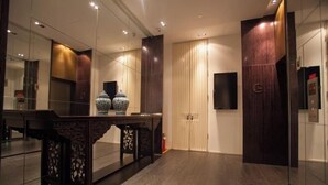 A modern hotel lobby with a dark wood floor, a large mirror, a decorative vase, and a closed door with a security camera. - Hotel MoMc (Beijing)