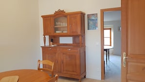 A wooden dining area with a table and chairs, a cabinet with glass doors, and a door leading to another room. - Provence: Crossing city apartment, quiet, very bright, terrace. 2 stars. (VALREAS)