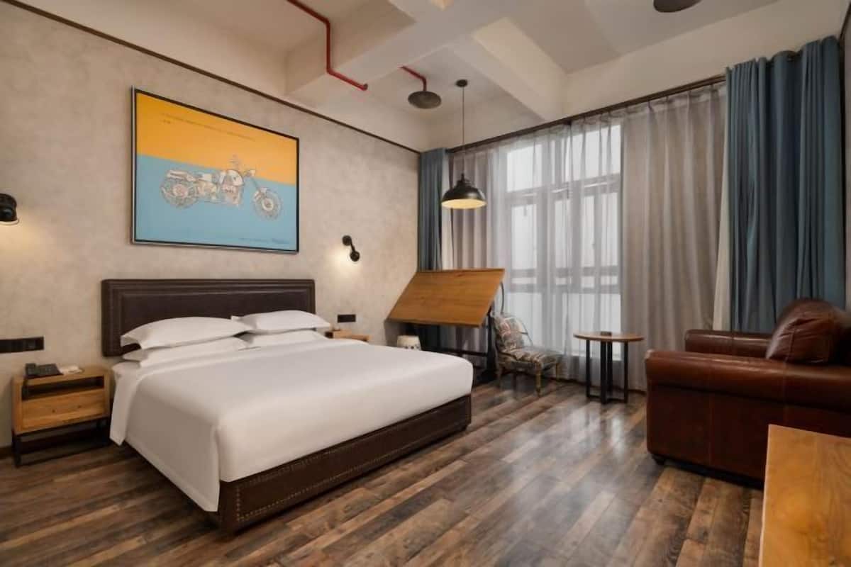 Una habitación de hotel moderna con una cama grande, suelo de madera, un escritorio, una silla y un sofá.